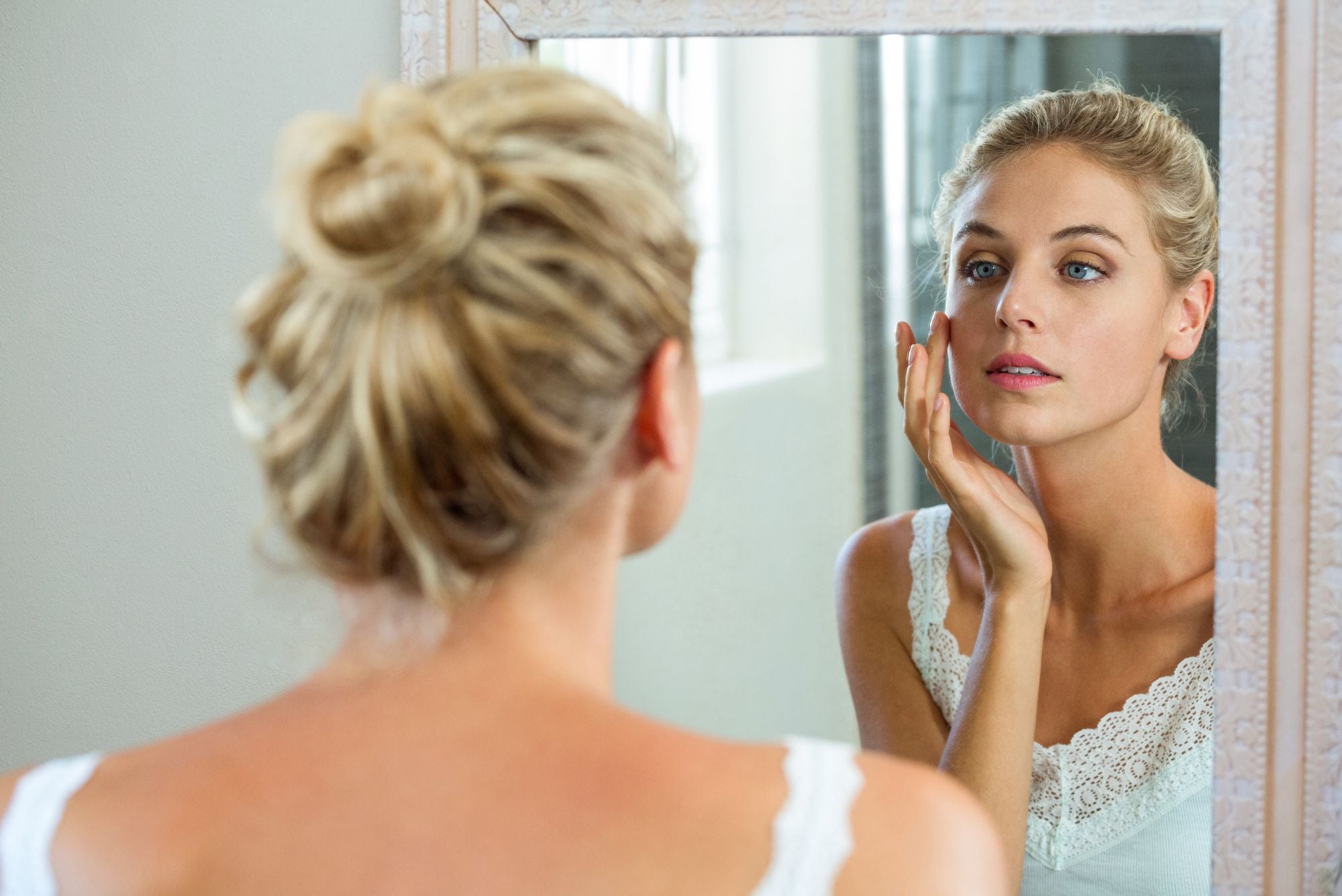 A woman looks in the mirror, touching her cheek and wondering, Does Neosporin help acne?
